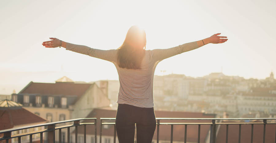 photo of woman standing on a sunny balcony with arms outstretched