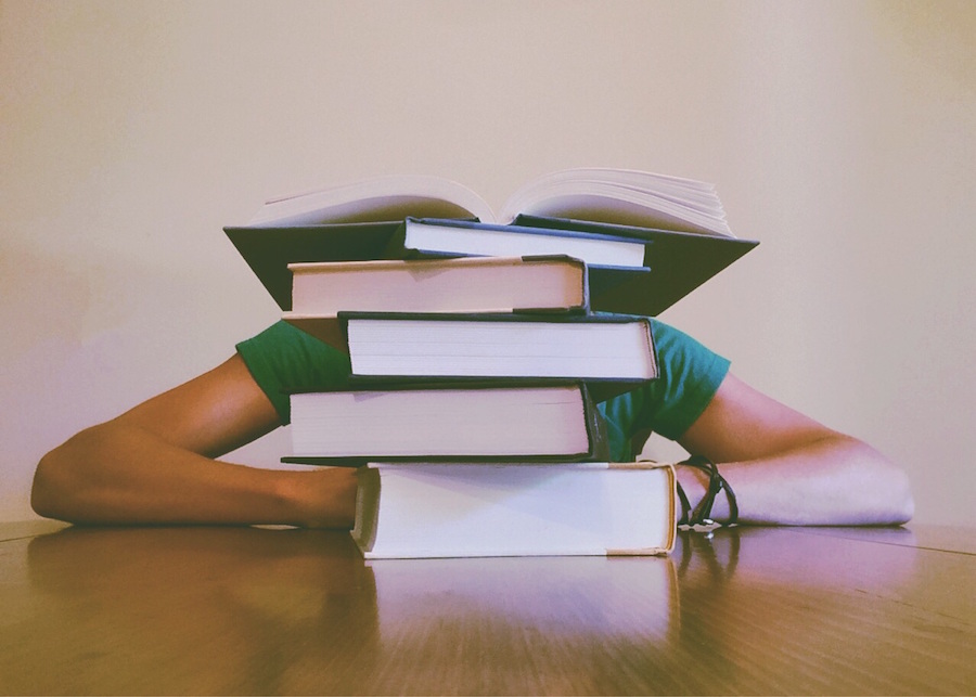Photo of a student doing research, hidden behind a big stack of books