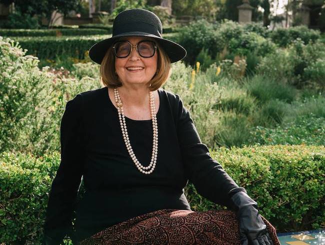 Photo of author Joan K. Lacy wearing a black shirt, black hat, black gloves, glasses and a pearl necklace.